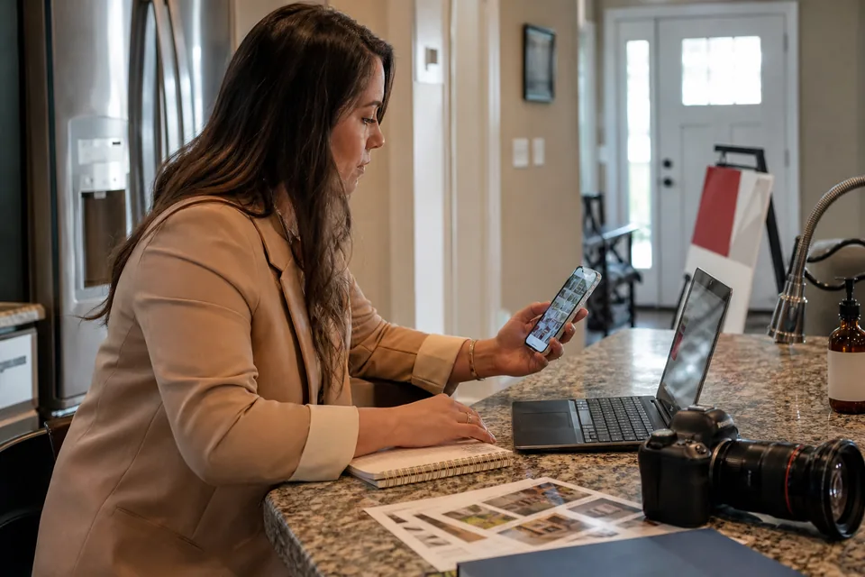 Real estate agent at a kitchen island in a staged listing, reviewing a social post draft on her phone