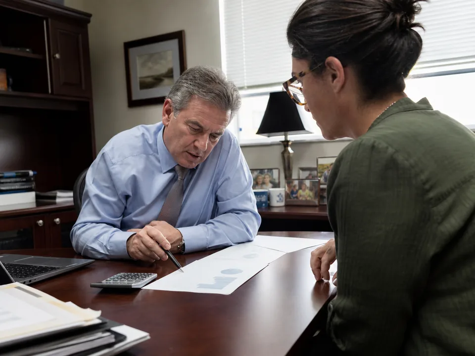 Financial advisor and his office manager comparing marketing subscription costs with a calculator at a conference table